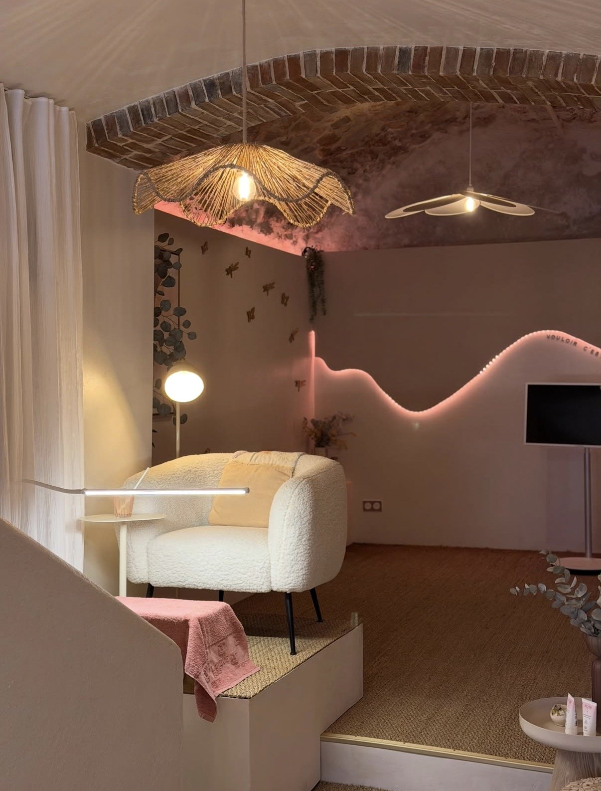 Vue d'ensemble de l'espace Pilates, lumière rose et suspensions en rotin.